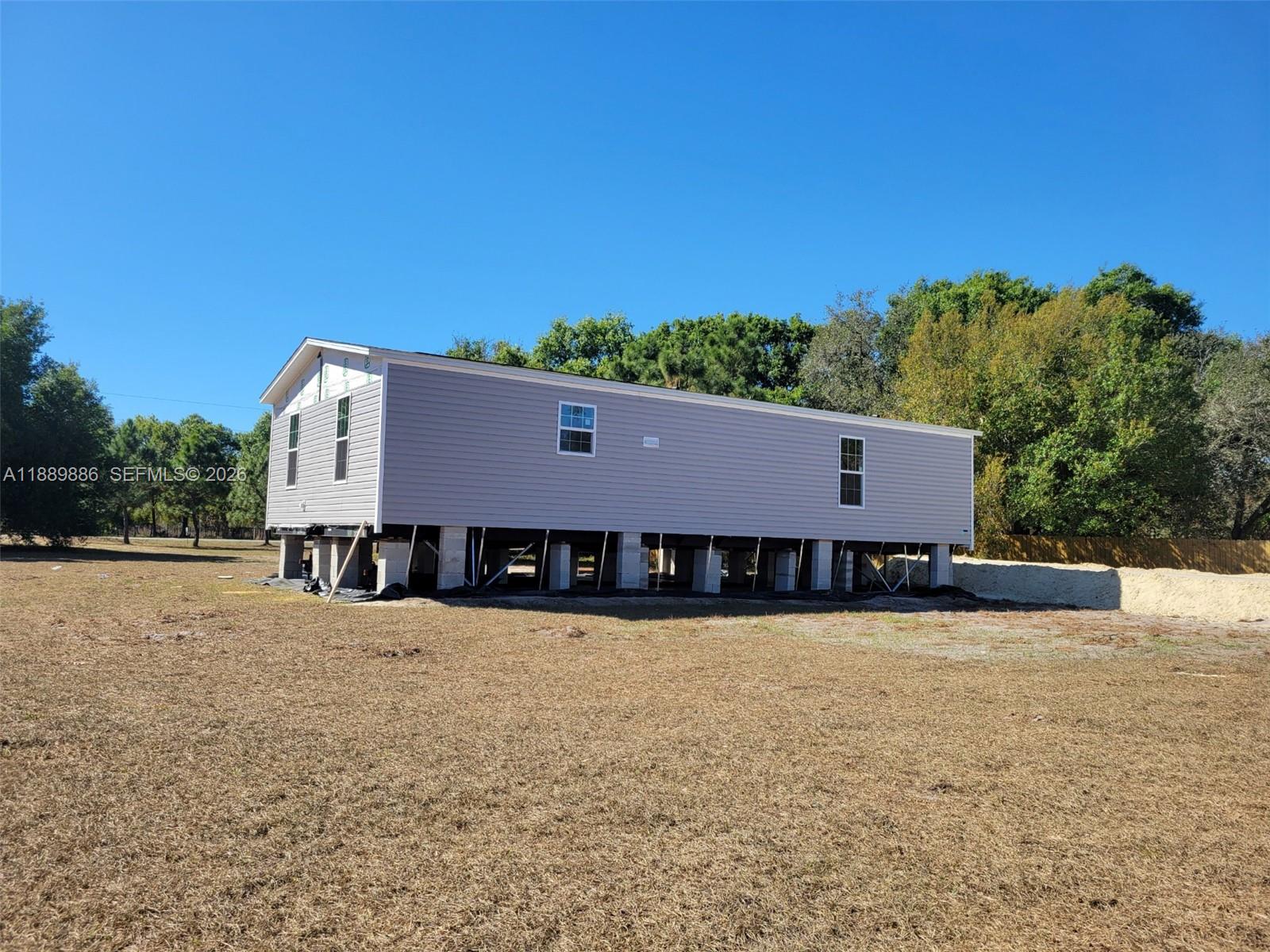 A light gray manufactured home sits on concrete block piers in a grassy field — 357 Horse Club, Clewiston FL 33440, CLEWISTON, FL