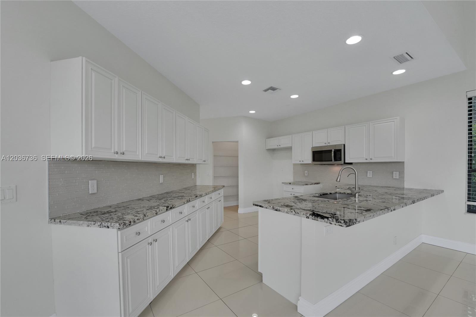A kitchen with white cabinets, granite countertops, a center island, and light tile flooring — 22281 Tupelo Pl, Boca Raton FL 33428, BOCA RATON, FL