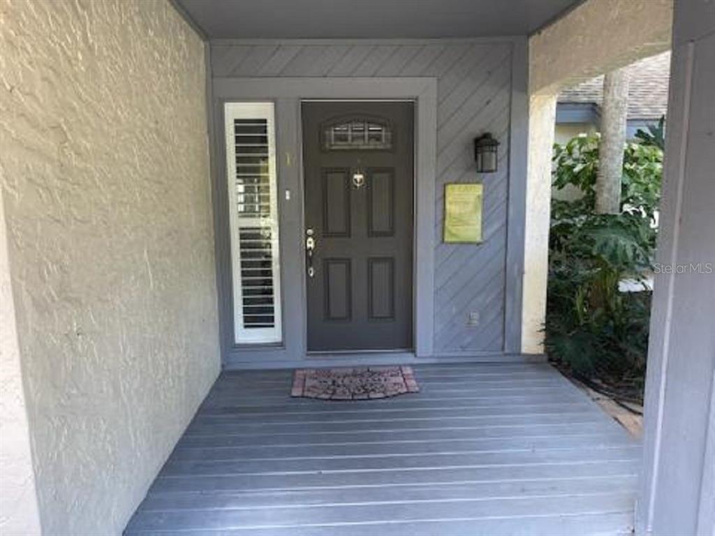 A dark gray front door with a side window sits on a covered wooden porch — 90 S HIGHLAND AVENUE UNIT 1, TARPON SPRINGS, FL
