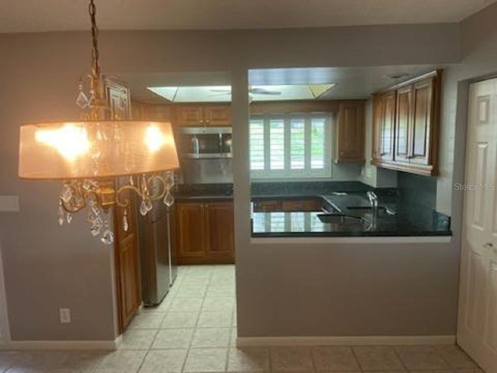 A kitchen with wood cabinets and dark countertops is viewed from an adjacent dining area — 90 S HIGHLAND AVENUE UNIT 1, TARPON SPRINGS, FL