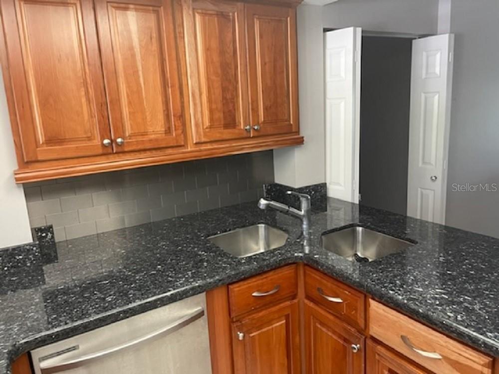 A kitchen features wood cabinets, dark granite countertops, a double-basin sink, and gray subway tile — 90 S HIGHLAND AVENUE UNIT 1, TARPON SPRINGS, FL