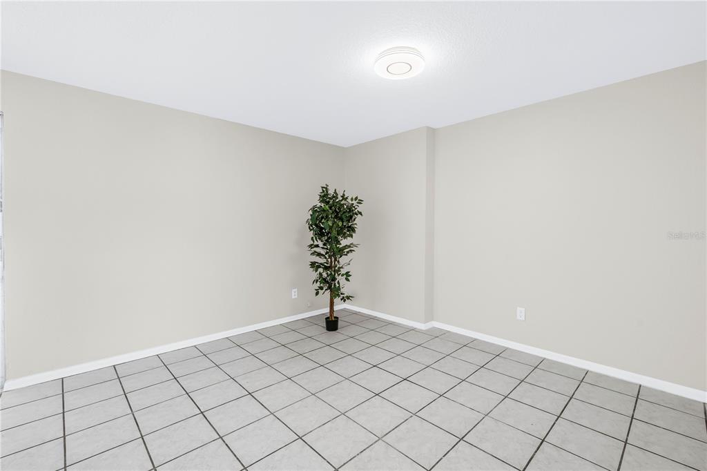 An empty room features light gray walls, a tiled floor, and a single potted plant — 10920 111TH STREET, LARGO, FL