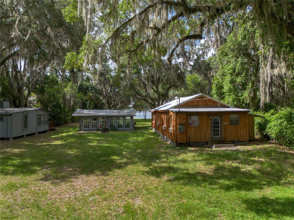 A wooden cabin and a separate small building sit on a grassy, tree-shaded lot — 1847 STATE ROAD 20, HAWTHORNE, FL