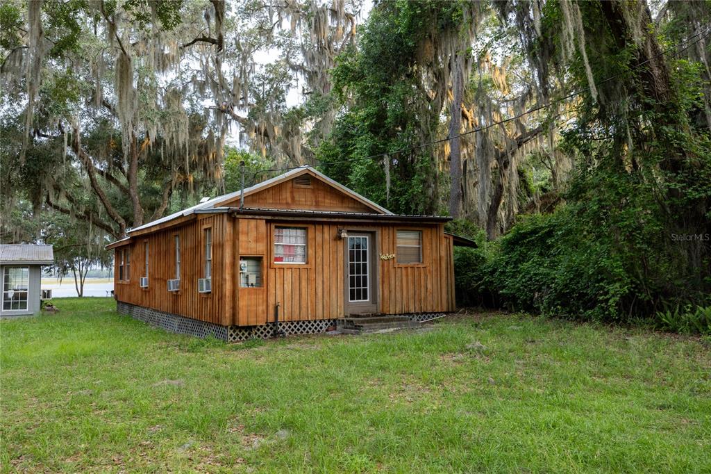 A rustic wooden cabin sits in a grassy yard surrounded by trees with hanging moss — 1847 STATE ROAD 20, HAWTHORNE, FL