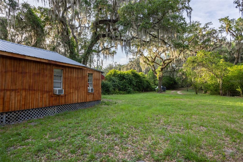 A wooden cabin with a metal roof sits on a grassy lot under large trees — 1847 STATE ROAD 20, HAWTHORNE, FL