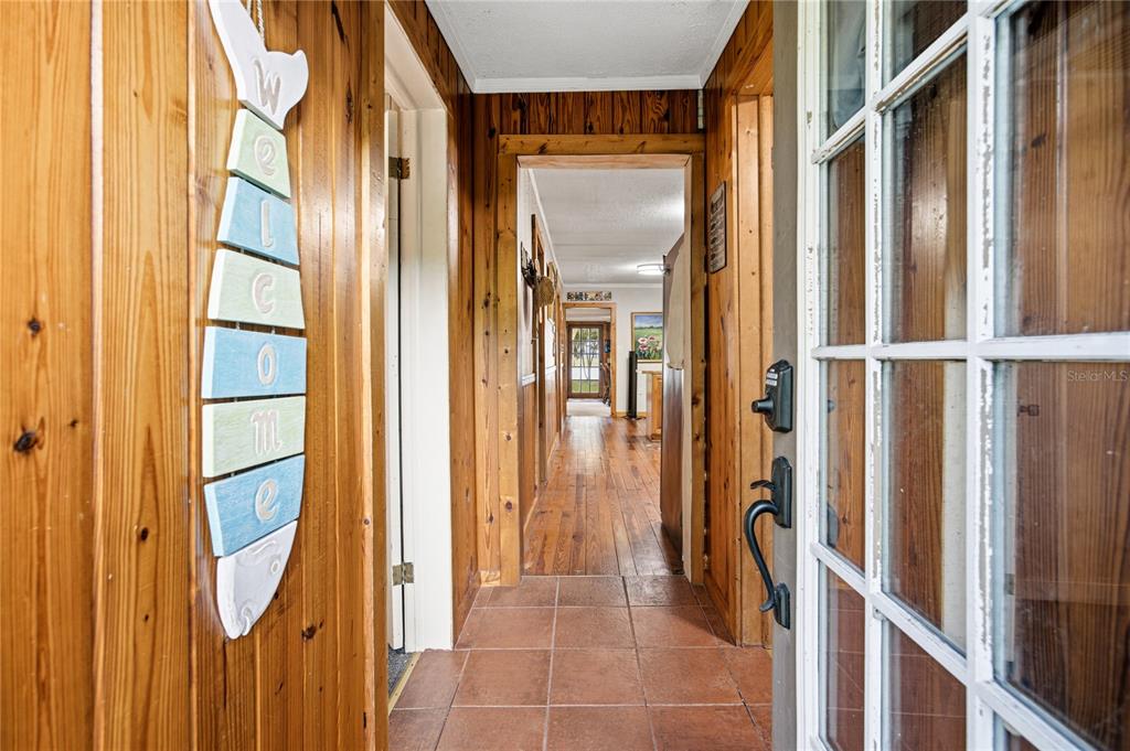 A hallway with wood-paneled walls, tile flooring, and a fish-shaped welcome sign leads indoors — 1847 STATE ROAD 20, HAWTHORNE, FL