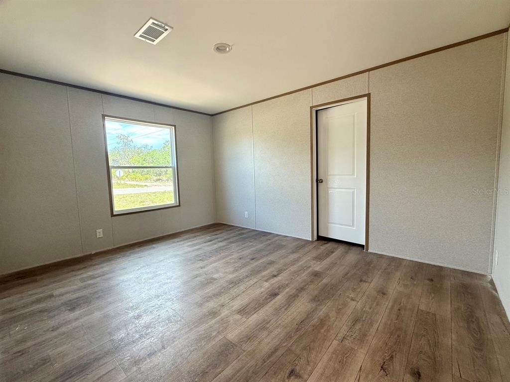 An empty room features light-colored paneled walls, wood-look flooring, a window, and a white door — TBD NE 115TH AVENUE, WILLISTON, FL
