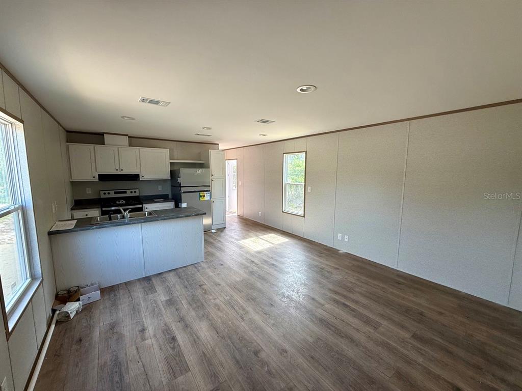 An open-concept kitchen and living area features light-colored walls and wood-look flooring — TBD NE 115TH AVENUE, WILLISTON, FL