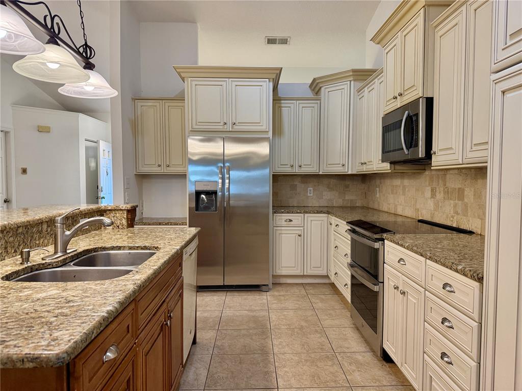 A kitchen features cream cabinets, granite countertops, stainless steel appliances, and a double sink — 1512 ISON LANE, OCOEE, FL