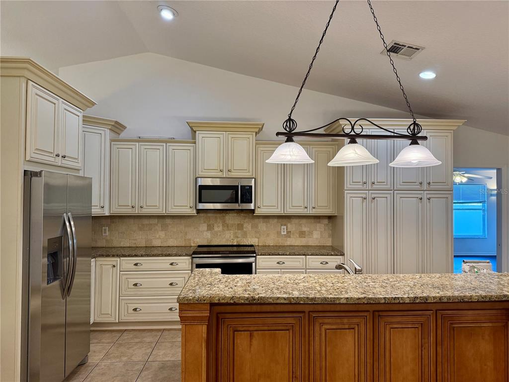 A kitchen features cream-colored cabinets, granite countertops, stainless steel appliances, and a wood-toned island — 1512 ISON LANE, OCOEE, FL