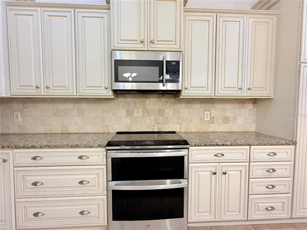 A kitchen features cream-colored cabinets, a stainless steel microwave, a double oven, and granite countertops — 1512 ISON LANE, OCOEE, FL