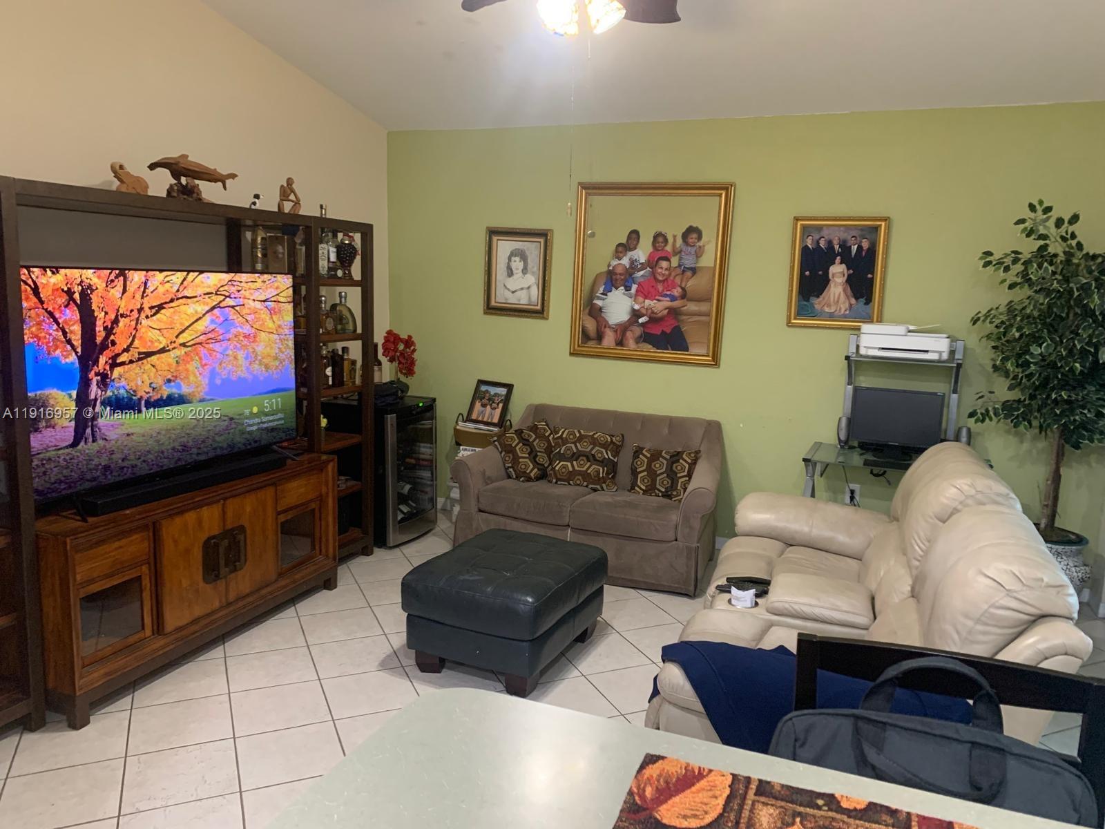 A living room features a large television, a beige sofa, and framed family portraits — 462 SE 23rd Dr, Homestead FL 33033, HOMESTEAD, FL