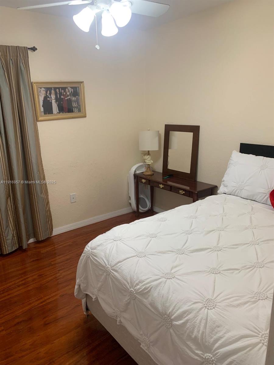A bedroom features a white tufted bed, a wooden vanity with a mirror, and hardwood floors — 462 SE 23rd Dr, Homestead FL 33033, HOMESTEAD, FL