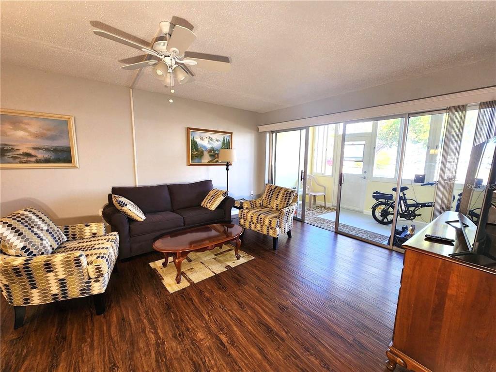 A living room features wood-look flooring, a dark sofa, patterned armchairs, and sliding glass doors — 21320 BRINSON AVENUE UNIT 109, PORT CHARLOTTE, FL