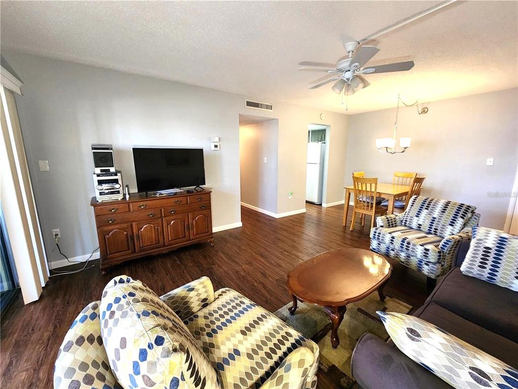 A living room with wood-look flooring, patterned armchairs, a wooden media console, and a dining area — 21320 BRINSON AVENUE UNIT 109, PORT CHARLOTTE, FL