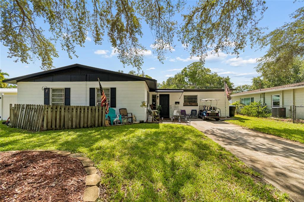 A single-story white house with a black roof, a wooden fence, and a driveway — 7846 12TH STREET N, ST PETERSBURG, FL