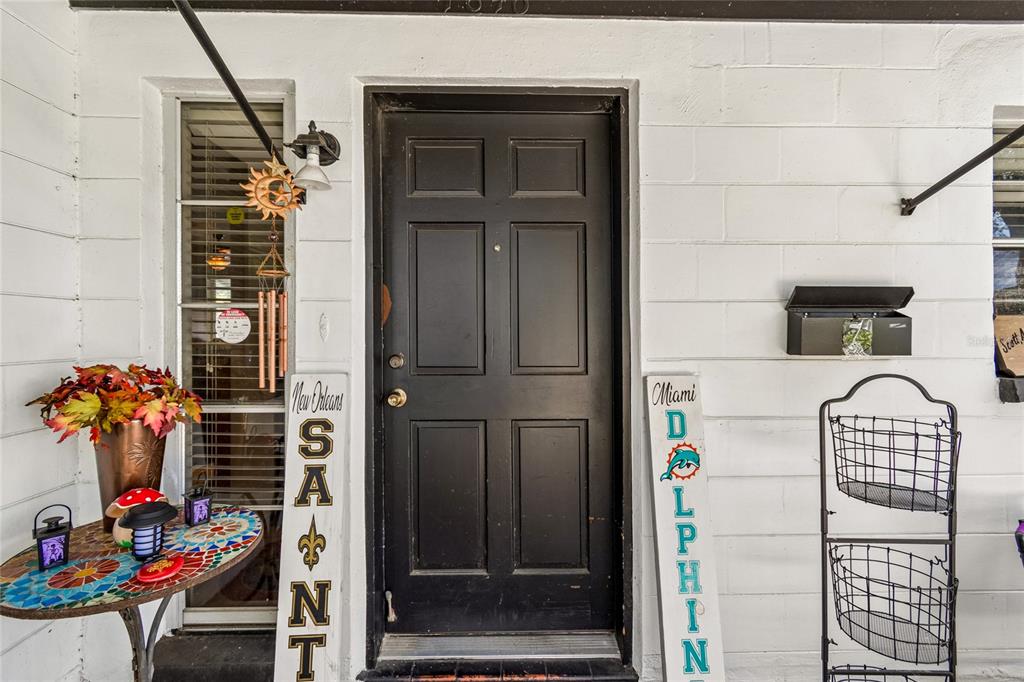 A black front door is flanked by decorative signs on a white painted brick porch — 7846 12TH STREET N, ST PETERSBURG, FL