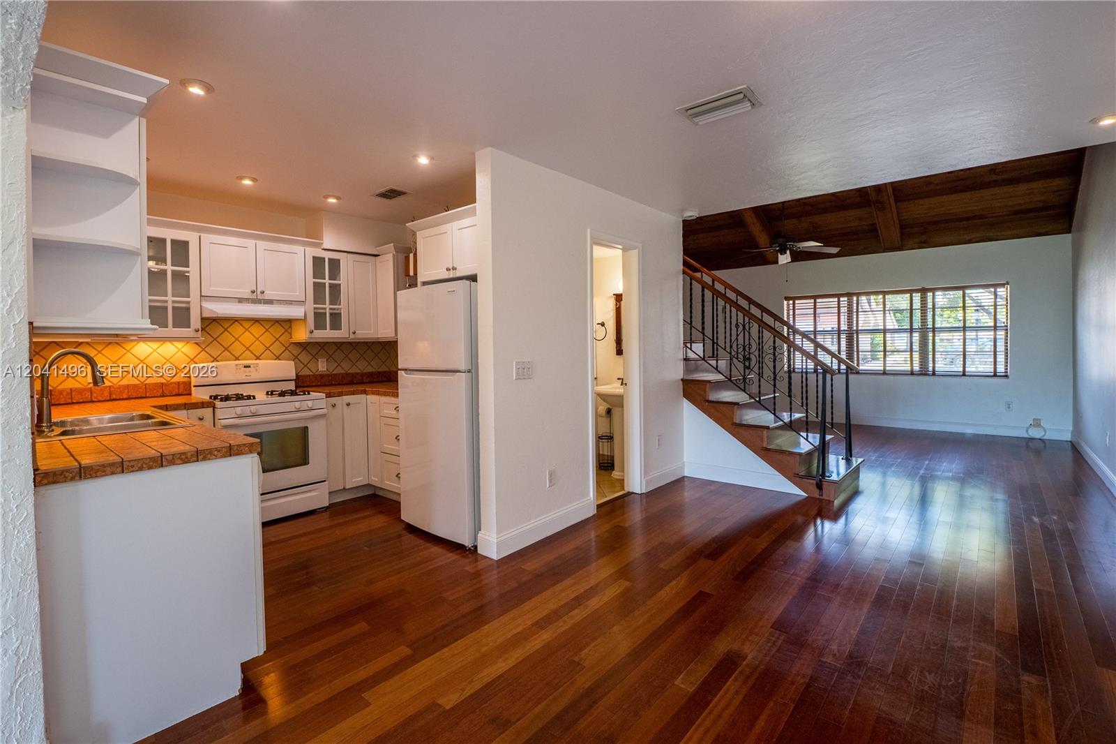 A kitchen with white cabinets and tile countertops opens to a living area with stairs — 2133 N 14th Ave, Hollywood FL 33020, HOLLYWOOD, FL