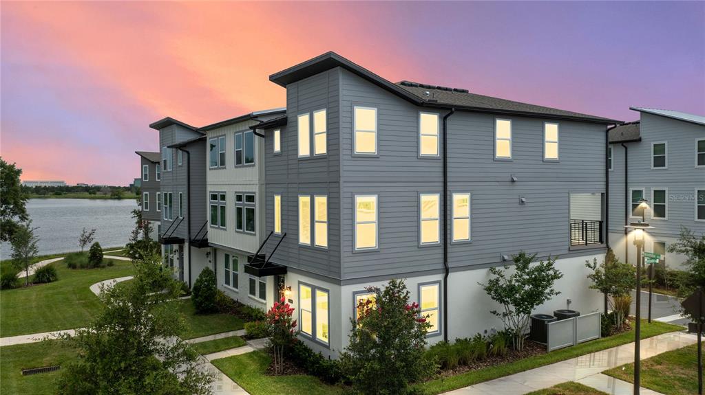 A three-story gray and white townhome exterior with a lake view at sunset — 12468 KOSHIBA ALLEY, ORLANDO, FL