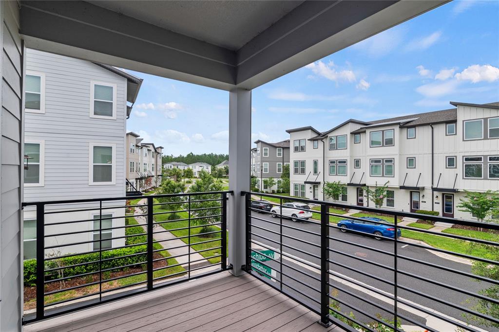 A covered balcony with a black metal railing overlooks a street and neighboring townhomes — 12468 KOSHIBA ALLEY, ORLANDO, FL