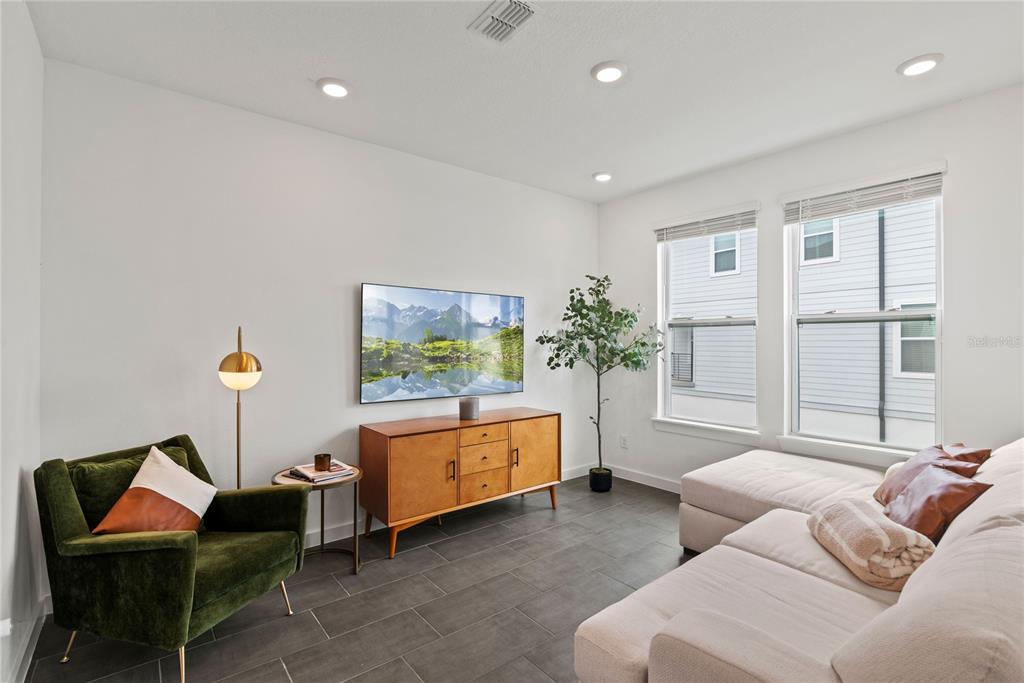 A living room features a green armchair, a wooden media console, and a light-colored sofa — 12468 KOSHIBA ALLEY, ORLANDO, FL