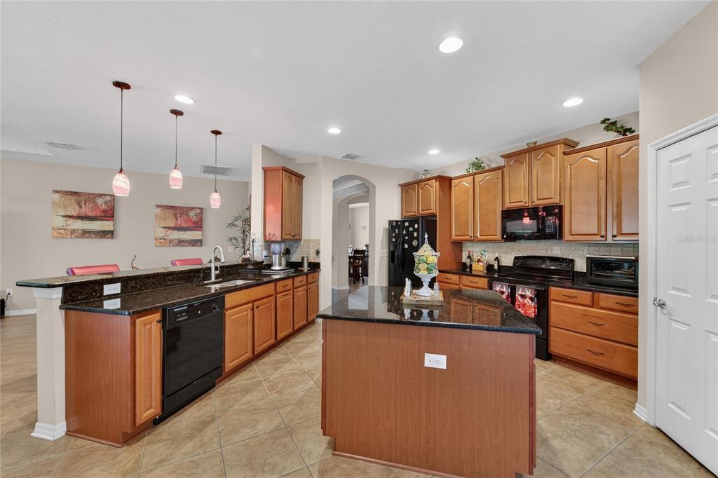 A kitchen features wood cabinets, dark granite countertops, a center island, and tile flooring — 12607 GENEVA GLADE DRIVE, RIVERVIEW, FL