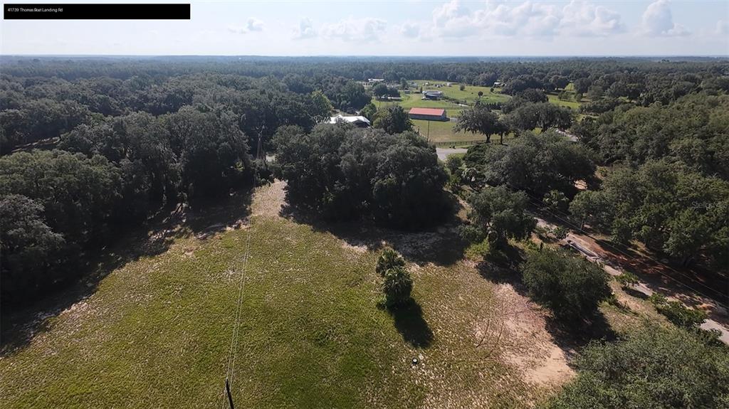 An aerial view shows a grassy field bordered by dense trees and a distant barn — 41739 THOMAS BOAT LANDING ROAD, UMATILLA, FL