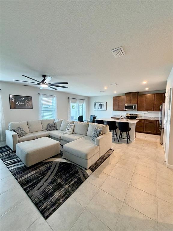 An open-concept living room features a large sectional sofa, tile flooring, and a kitchen area — 35550 SPARROW NEST WAY, ZEPHYRHILLS, FL