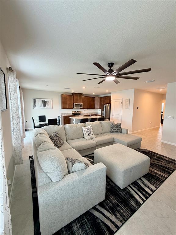 A living room with a sectional sofa and ottoman opens to a kitchen and dining area — 35550 SPARROW NEST WAY, ZEPHYRHILLS, FL