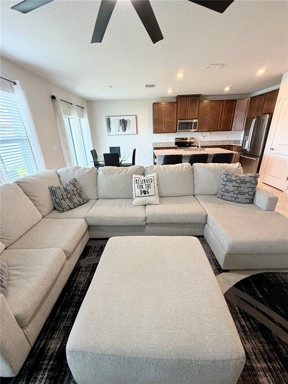 A living room with a large sectional sofa and ottoman opens to a kitchen area — 35550 SPARROW NEST WAY, ZEPHYRHILLS, FL