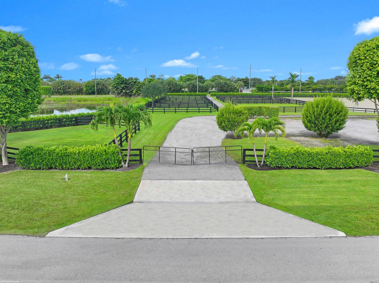A paved driveway leads through a gated entrance into a fenced equestrian property with landscaping — 3899 Shutterfly Way, Wellington FL 33414, WELLINGTON, FL