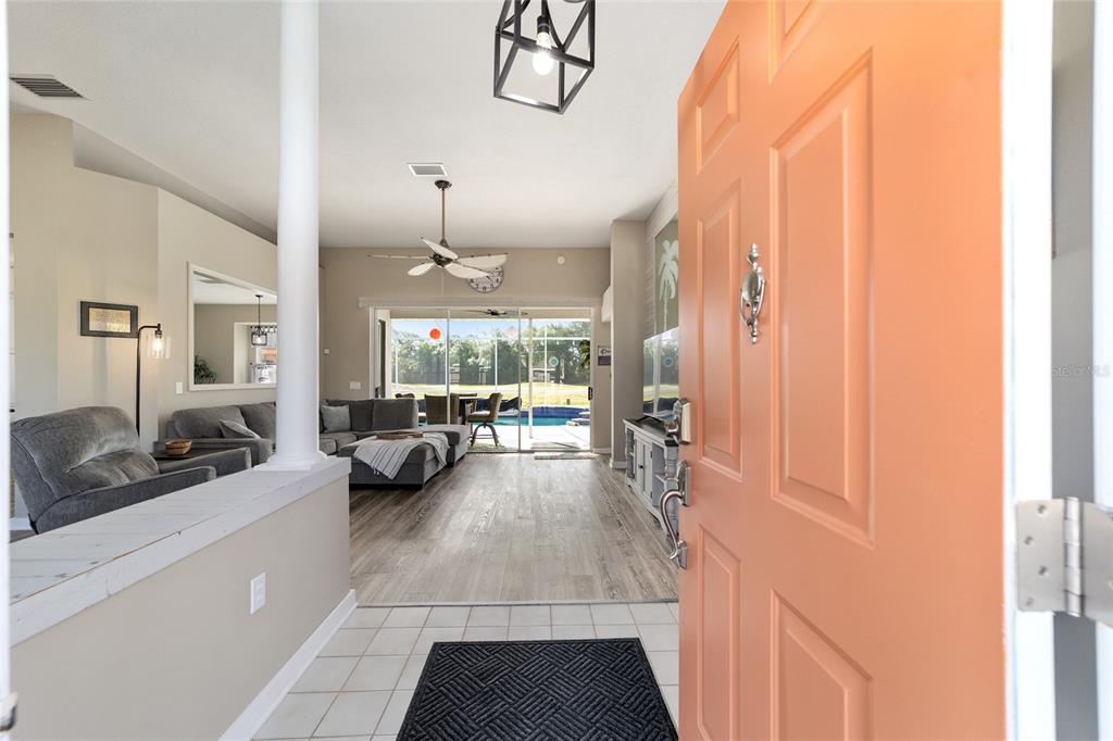 An open-concept living room with wood-look flooring, a pool view, and a coral front door — 4543 N JADEMOOR DRIVE, BEVERLY HILLS, FL