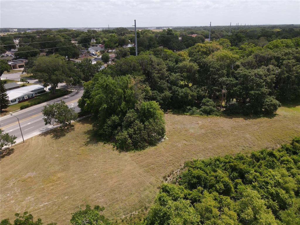 An aerial view shows a grassy vacant lot bordered by trees and a paved road — NEPTUNE ROAD, KISSIMMEE, FL