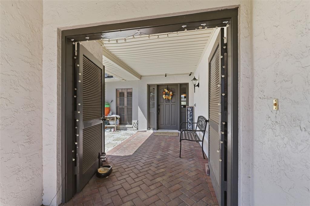 A brick-paved courtyard entrance features louvered doors, a bench, and a dark front door — 12935 RAIN FOREST STREET, TEMPLE TERRACE, FL