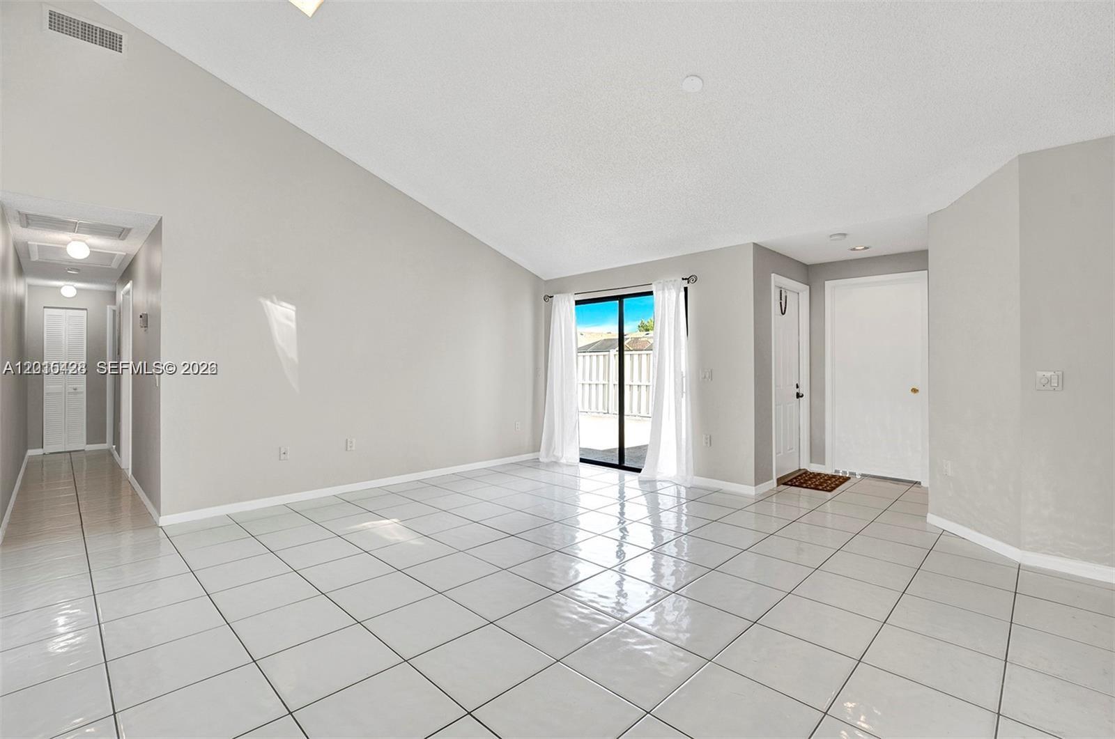 A bright, empty living room features white tile floors, vaulted ceilings, and sliding glass doors — 9892 Boca Gardens Pkwy # A, Boca Raton FL 33496, BOCA RATON, FL