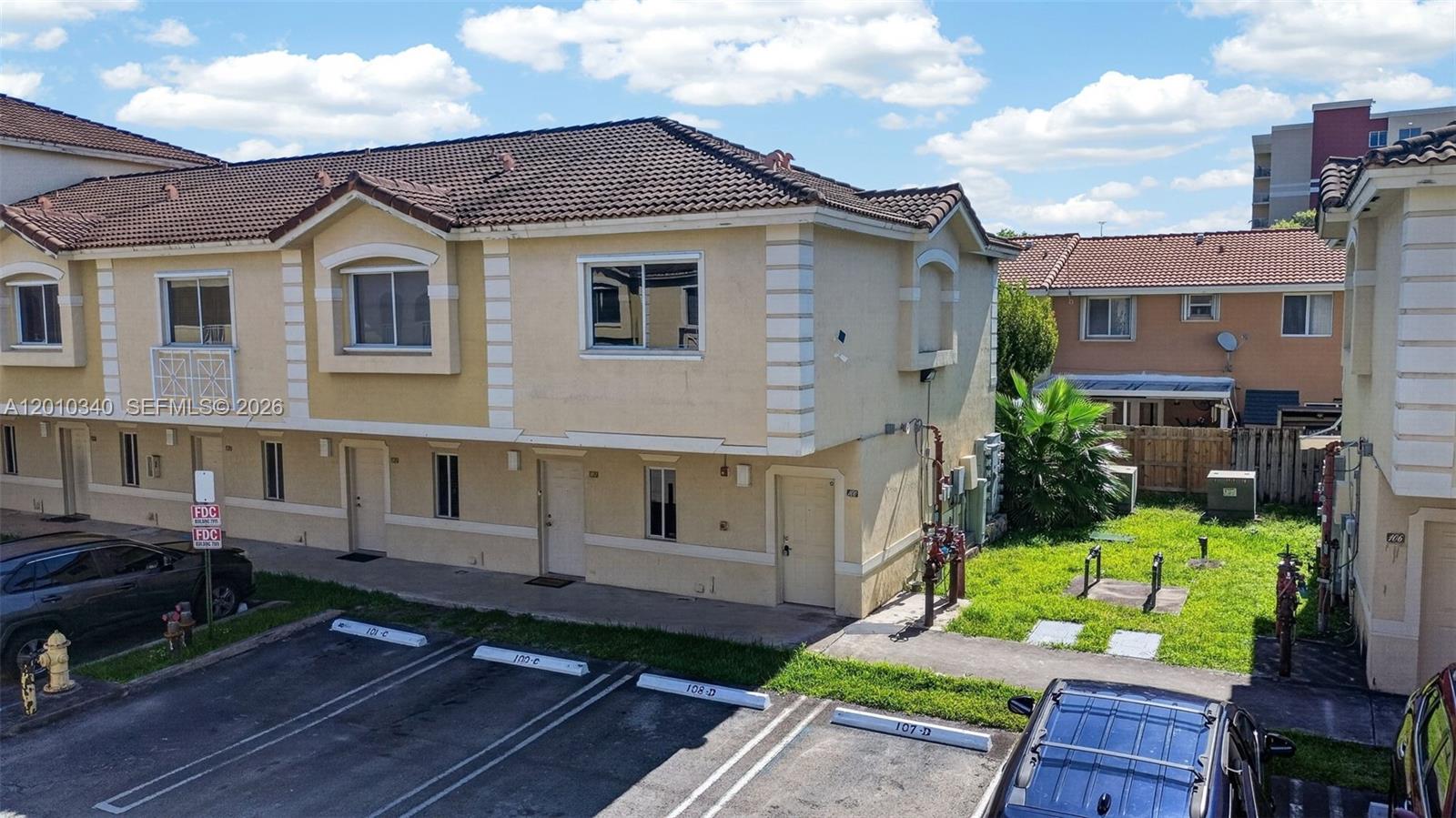 An exterior view of a two-story tan townhouse complex with parking spaces in front — 7995 NW 8th St # 100C, Miami FL 33126, MIAMI, FL