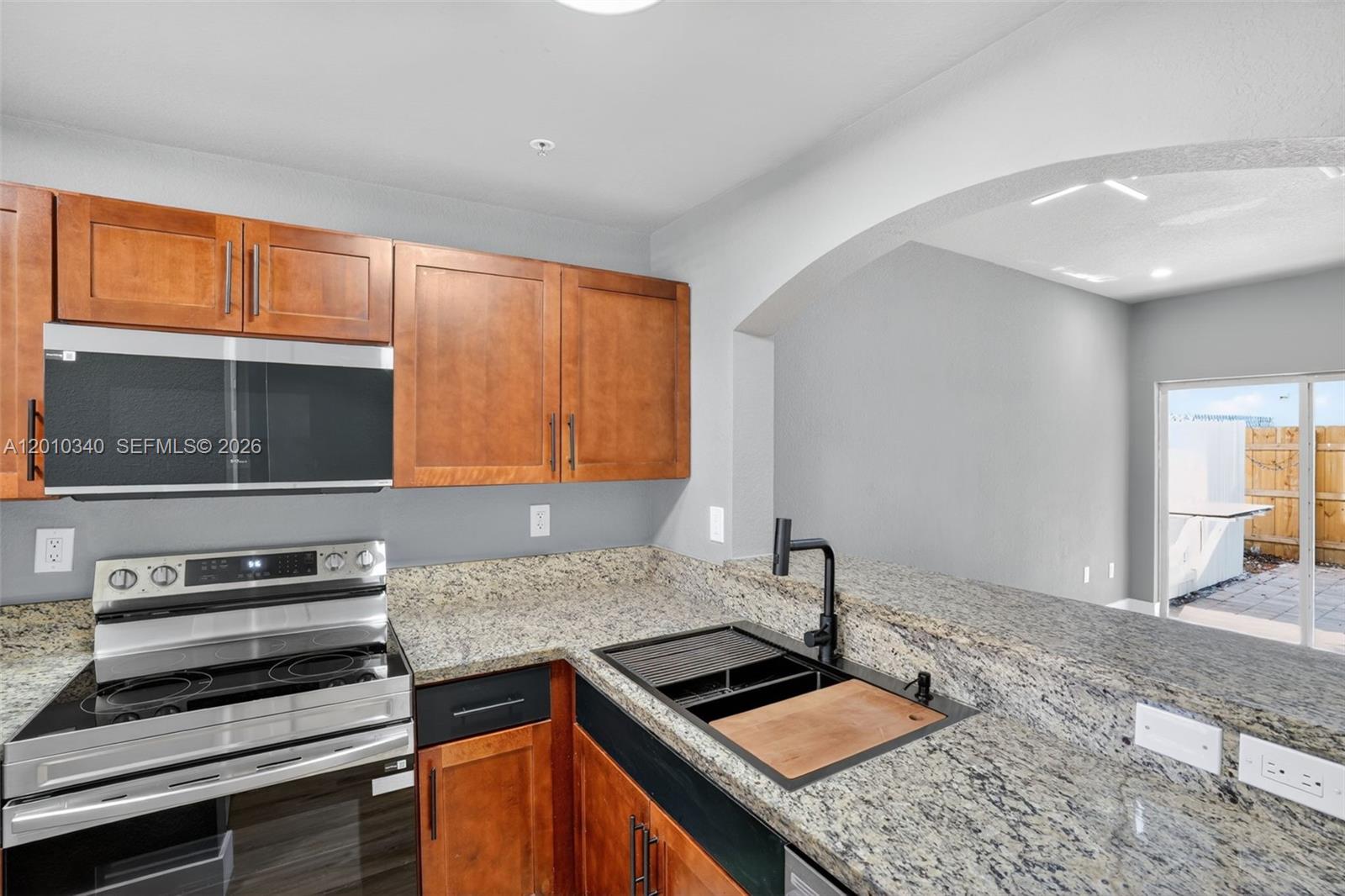 A kitchen features granite countertops, wood cabinets, a stainless steel stove, and a black sink — 7995 NW 8th St # 100C, Miami FL 33126, MIAMI, FL