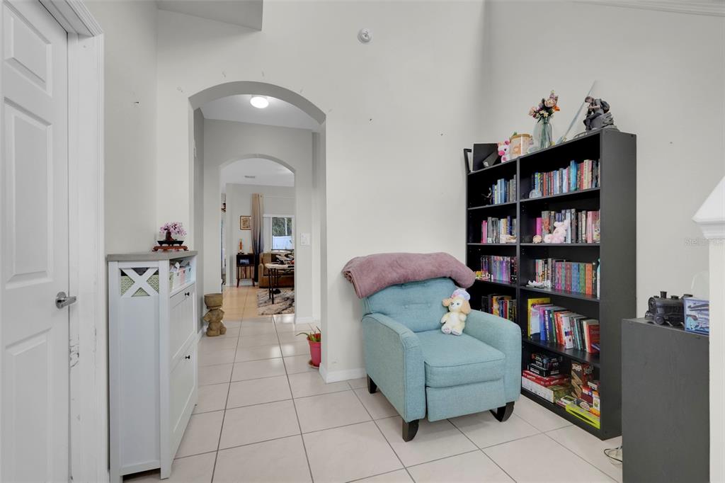 A light-colored tiled hallway features an arched entryway, a blue armchair, and a black bookshelf — 4384 PARADISE COVE COURT, KISSIMMEE, FL