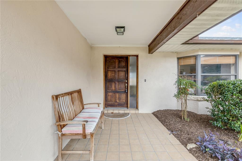 A covered front porch features a wooden bench, tiled flooring, and a dark wood door — 45 WEBSTER LANE, PALM COAST, FL