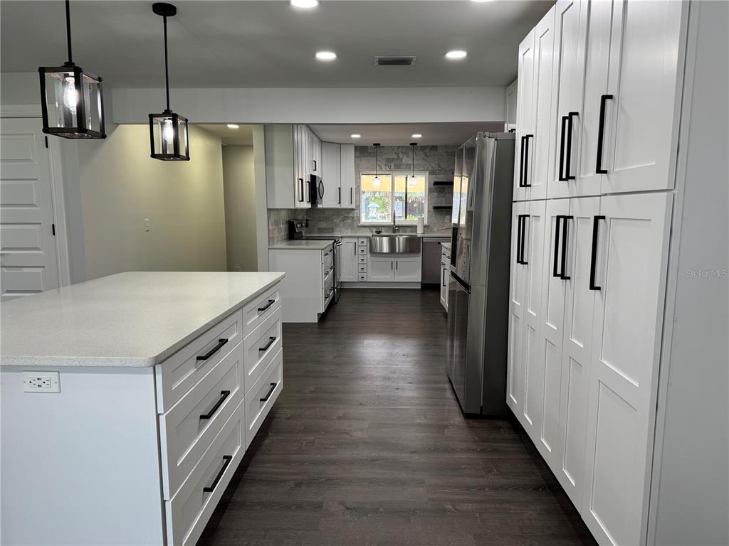 A modern kitchen features white cabinetry, a large island, stainless steel appliances, and dark flooring — 1809 STELLA COURT N, LAKELAND, FL