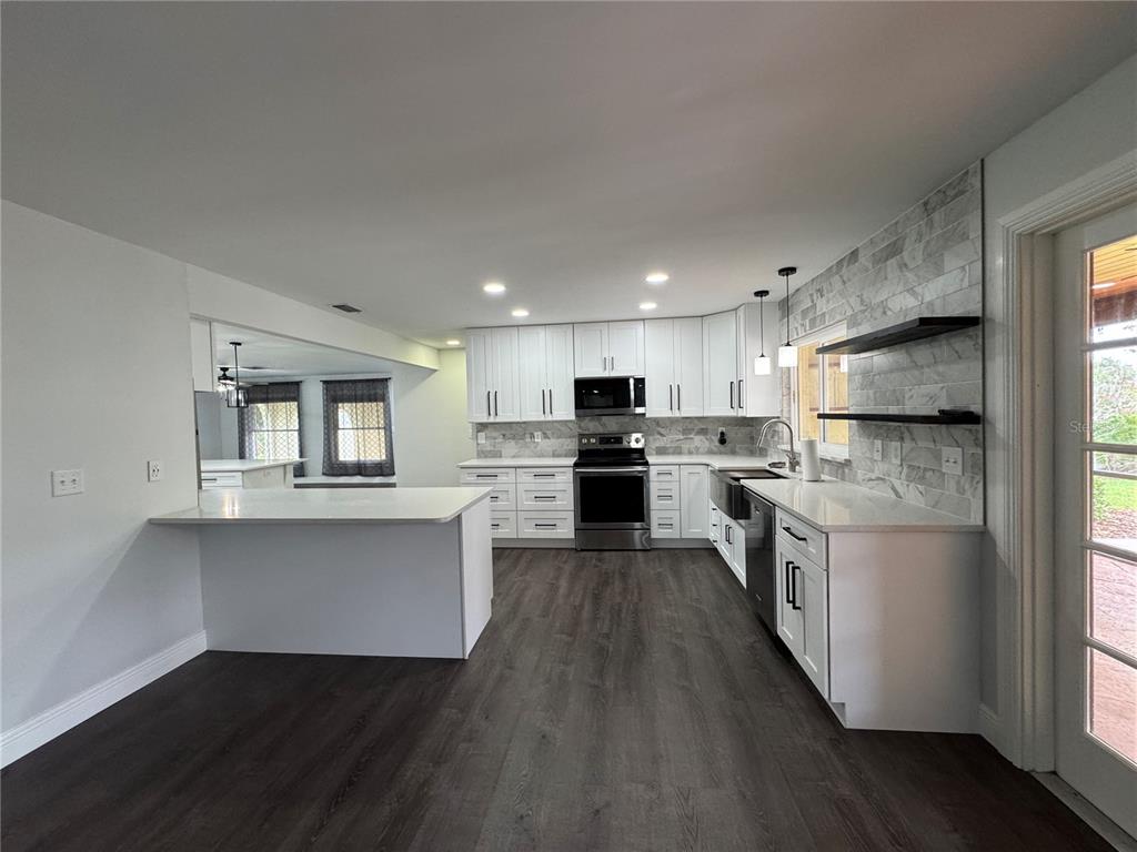 A modern kitchen features white cabinets, stainless steel appliances, marble-style backsplash, and dark wood flooring — 1809 STELLA COURT N, LAKELAND, FL