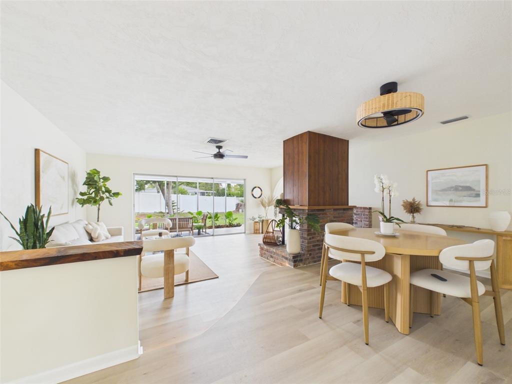 An open-concept living and dining area features light wood flooring and a central brick fireplace — 533 66TH STREET N, PALM HARBOR, FL