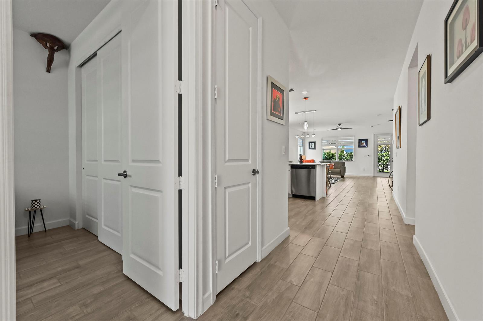 A hallway with light wood-look tile flooring leads toward an open-concept kitchen and living area — 13451 Noble Drive, Delray Beach FL 33484, DELRAY BEACH, FL