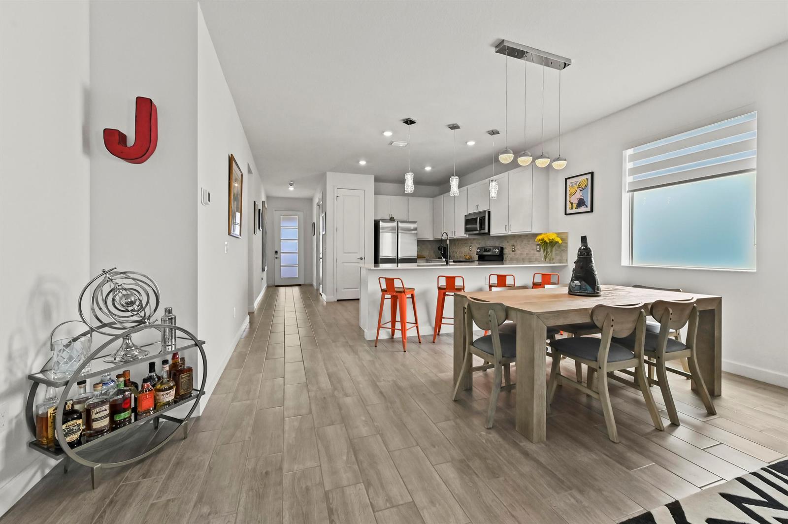 A modern open-concept kitchen and dining area features white cabinetry, orange barstools, and wood flooring — 13451 Noble Drive, Delray Beach FL 33484, DELRAY BEACH, FL