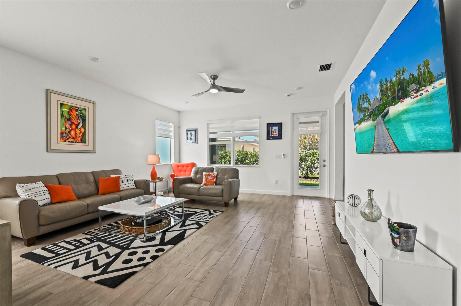 A living room features a grey sofa, patterned rug, white media console, and wall-mounted television — 13451 Noble Drive, Delray Beach FL 33484, DELRAY BEACH, FL
