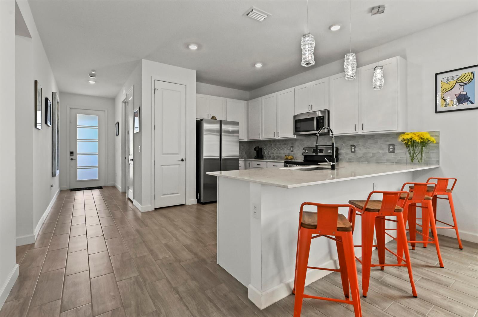 A modern kitchen features white cabinetry, stainless steel appliances, a quartz island, and orange barstools — 13451 Noble Drive, Delray Beach FL 33484, DELRAY BEACH, FL