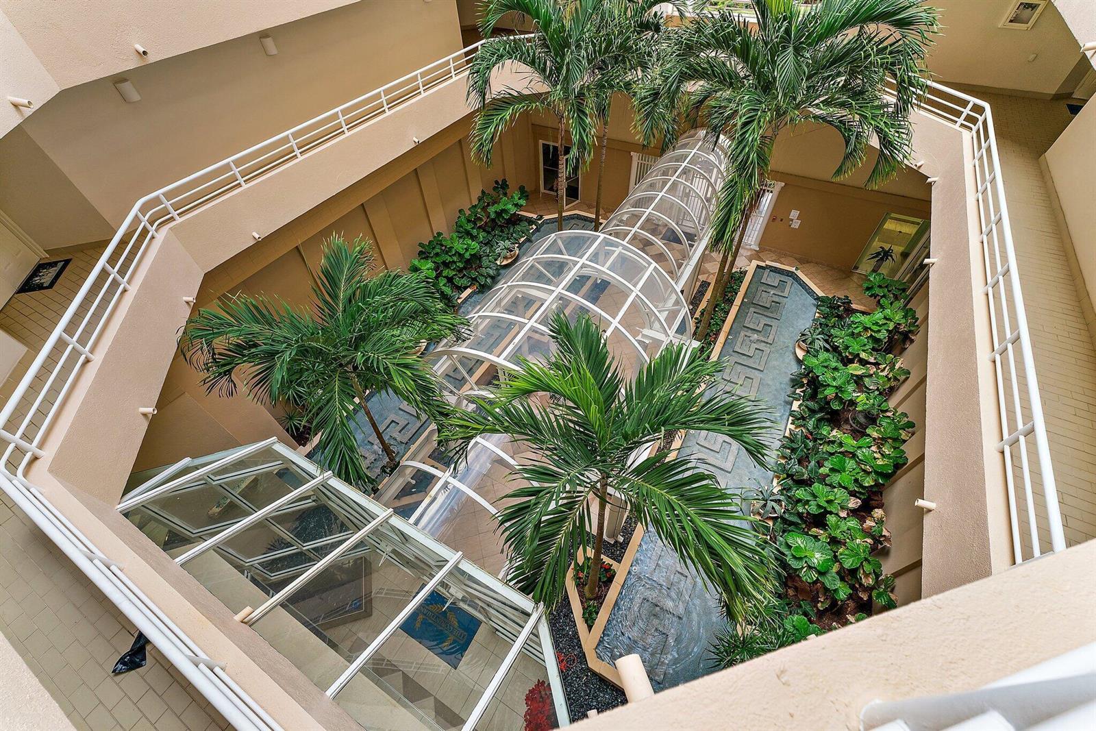 An elevated view of an indoor atrium featuring palm trees, a glass-roofed walkway, and landscaping — 176 Helios Drive # 606, Jupiter FL 33477, JUPITER, FL