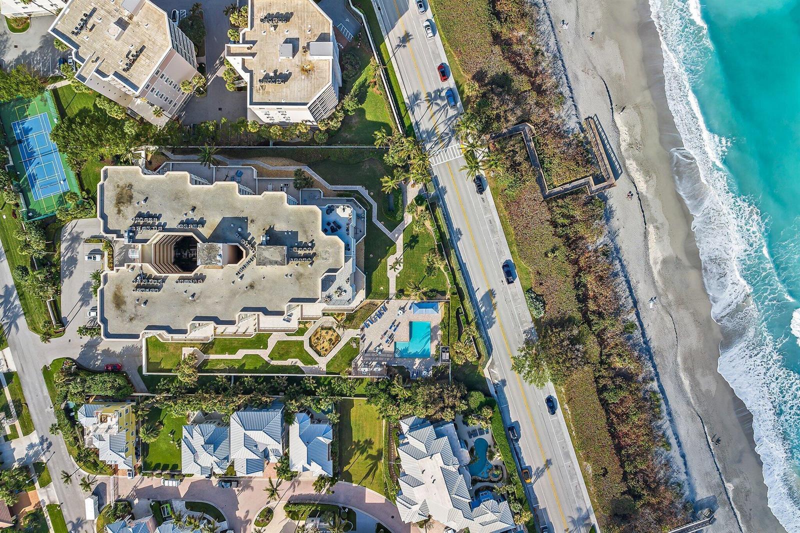 An aerial view shows a coastal condominium complex with a pool, tennis court, and beach — 176 Helios Drive # 606, Jupiter FL 33477, JUPITER, FL