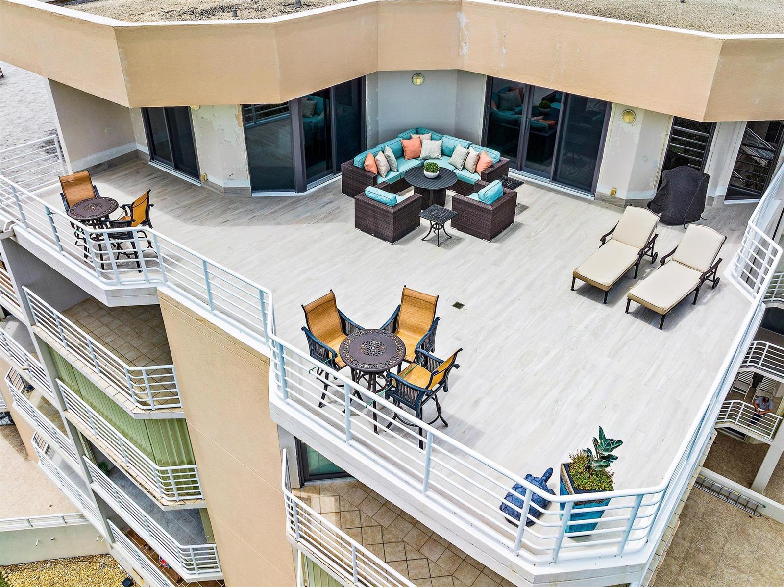 An elevated outdoor terrace features patio furniture, lounge chairs, and light-colored wood-look flooring — 176 Helios Drive # 606, Jupiter FL 33477, JUPITER, FL
