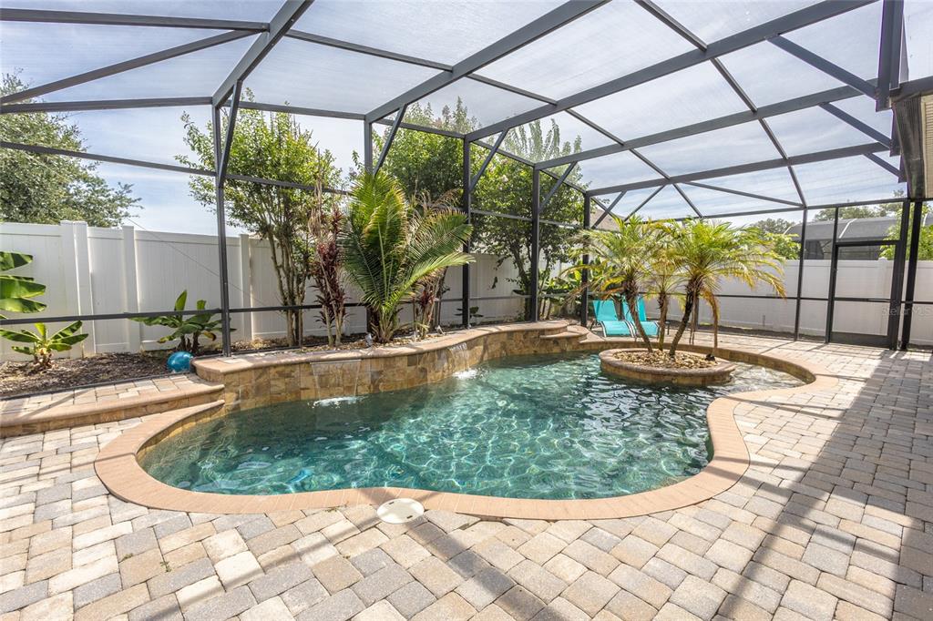 A screened-in patio features a freeform swimming pool with a stone-tiled wall and central island — 4925 TORTOISE TRAIL, ST CLOUD, FL